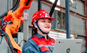 Female engineer with laptop overseeing robotic arm in a manufacturing setting in Vietnam.
