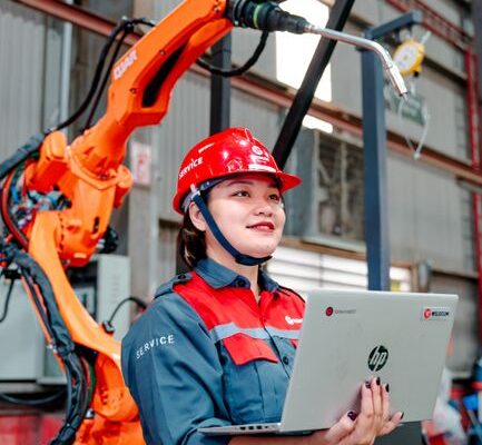 Female engineer with laptop overseeing robotic arm in a manufacturing setting in Vietnam.