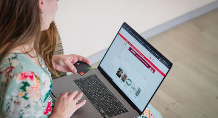 Woman in floral dress shopping online with a laptop and credit card indoors.